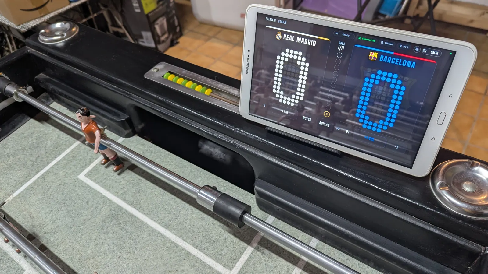 La tablet con el marcador a 0-0, apoyada en el futbolín junto al ábaco